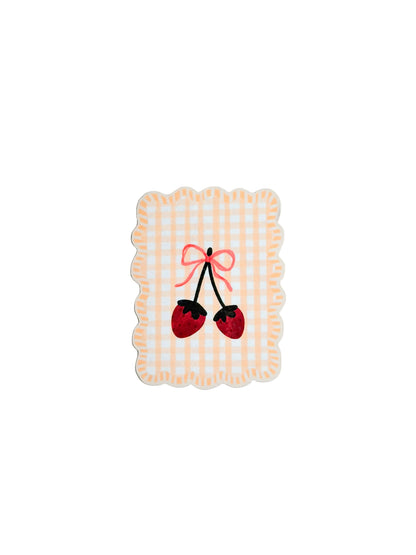 Decorative coaster with cherries and a bow on a checkered pattern against a light blue background